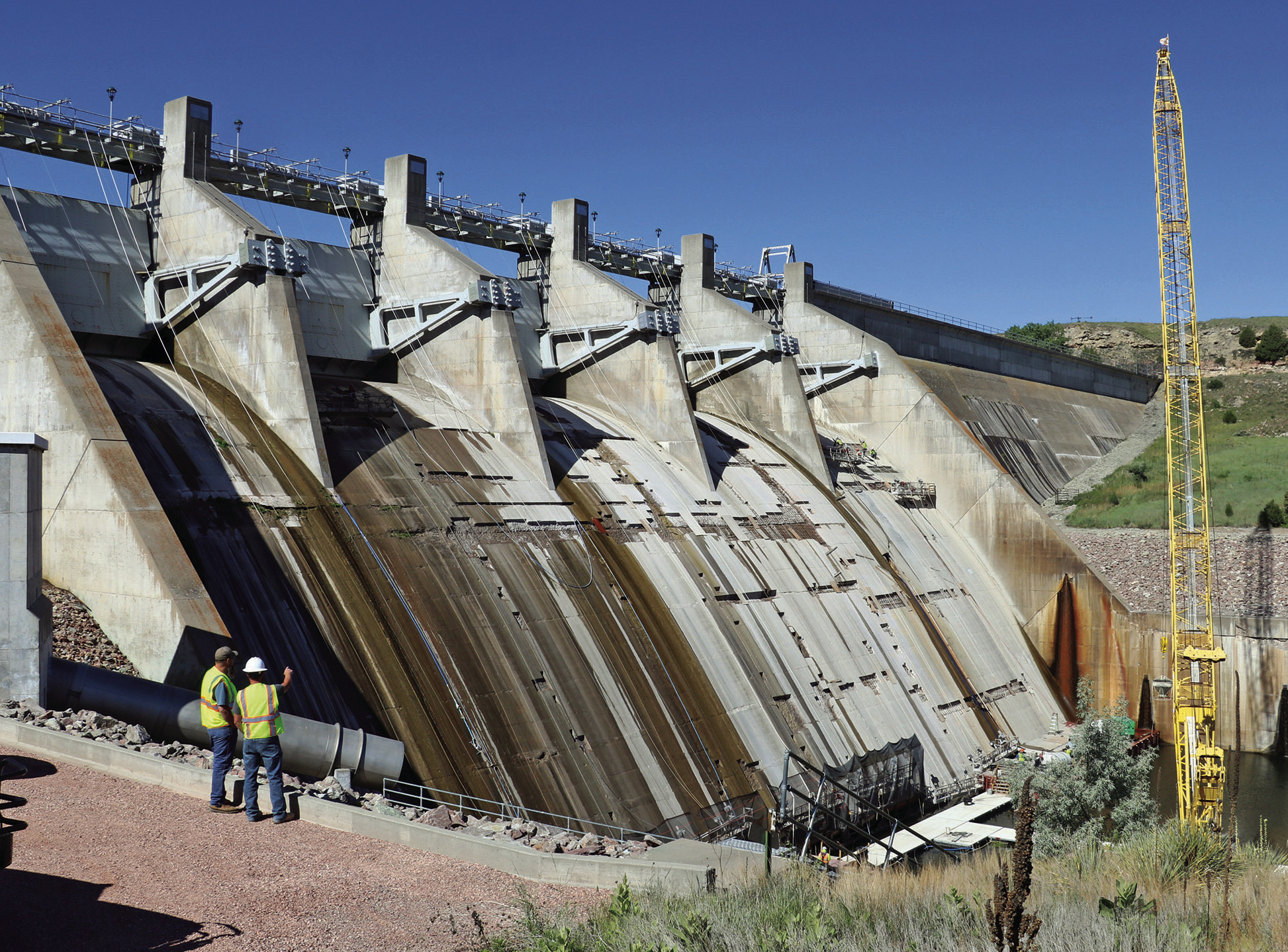 Angostura Dam Tender R.J. Wright, lower left, and Steven Fritch with the U.S. Bureau of Reclamation, stand above the work area and observe crews repairing concrete on the face of the dam. Photo by Brett Nachtigall/Fall River County Herald-Star