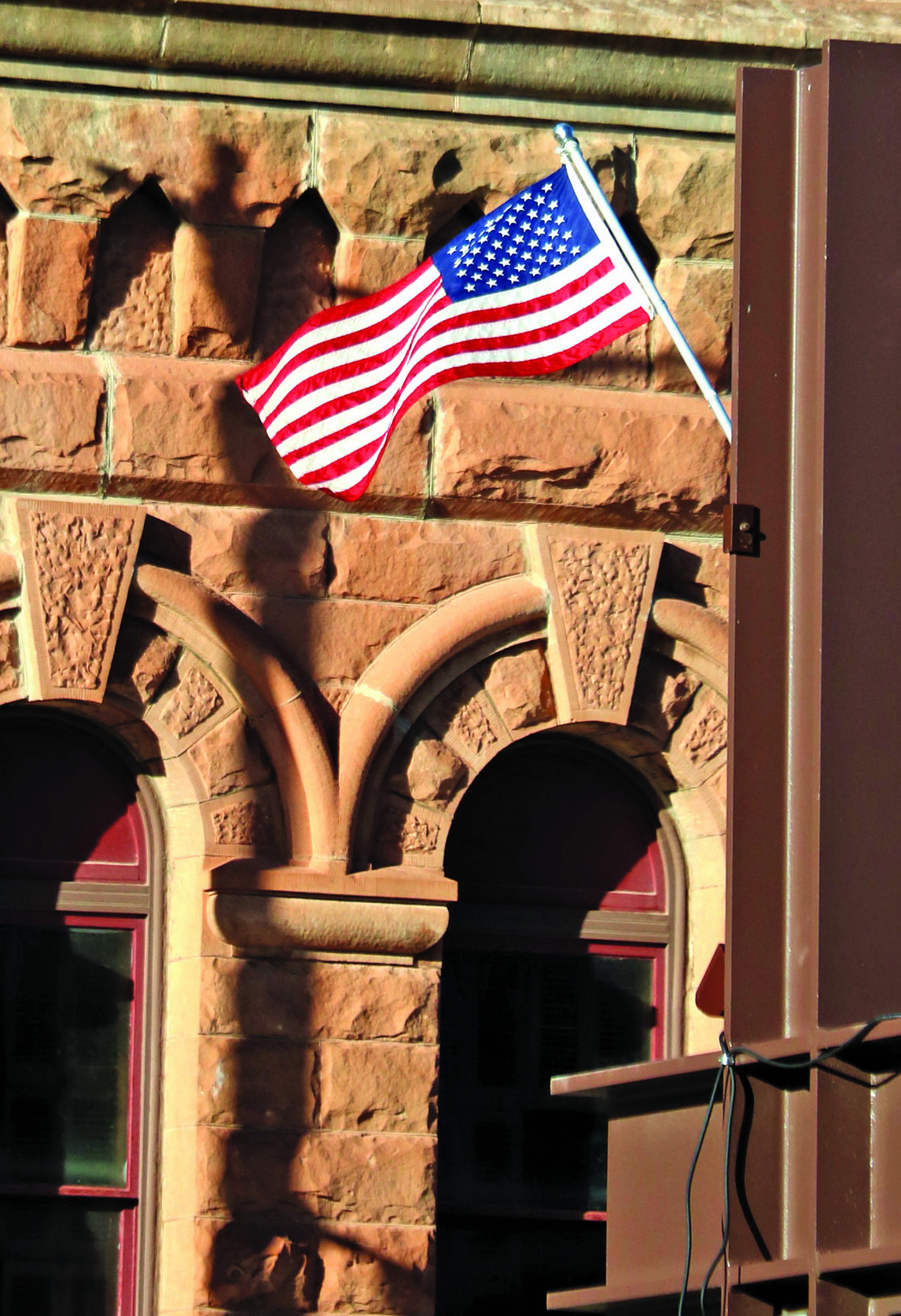 An American Flag waves from the North River Street suspended sidewalk in Hot Springs as the sandstone architecture of City Hall provides a beautiful backdrop for this scene in The Veterans Town. Photo by Brett Nachtigall/Fall River County Herald-Star