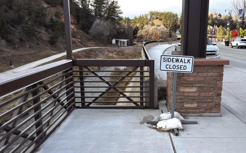 A ‘Sidewalk Closed” sign sits on the north end of the downtown suspended sidewalk due to a design flaw that placed a tower directly in the middle of the transition point leading to the regular sidewalk on the west side of North River Street. Photo by Brett Nachtigall/Fall River County Herald-Star
