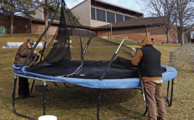 Jake McClure and his family retrieve their trampoline from in front of The Mammoth Site on Thursday morning, following the wind storm the previous night. The McClures live about a block away and were not the only ones whose personal property ended up trapped near the prehistoric sink hole, as a large steel carport was also found upside down nearby as well. Photo by Brett Nachtigall/Fall River County Herald-Star