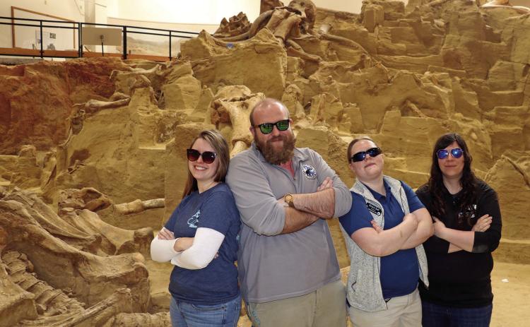 While wearing sunglasses, four paleontologists at The Mammoth Site pose for a photo inside the facilty’s bonebed area. Pictured from left is Kelly Lubbers, Seth Vandenberg, Grace Self and Alex Gardner. Photo by Brett Nachtigall/Fall River County Herald-Star