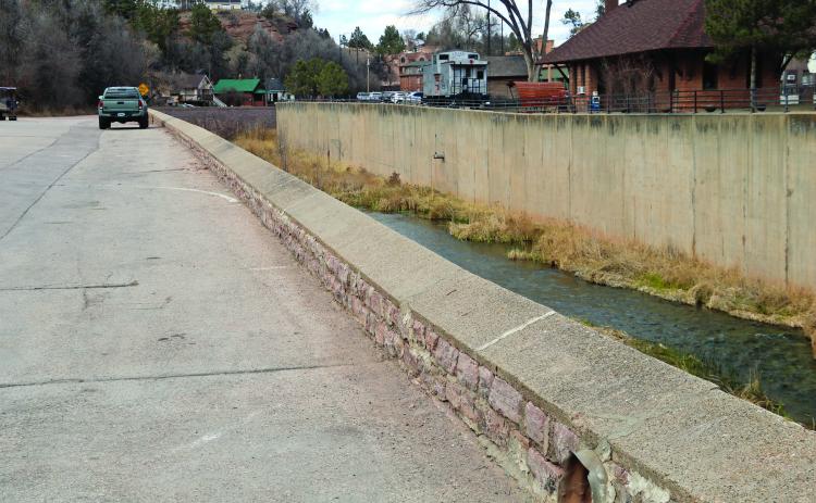 At its lowest end, the river channel retaining wall in front of the Springs Lodge and Cafe is just 18-inches tall, as shown here. On the opposite side of the river, there is a higher railing (shown in the top of the photo) located behind the Depot Visitor’s Center. The City of Hot Springs is currently contemplating between permanent and temporary solutions to the issue. Photo by Brett Nachtigall/Fall River County Herald-Star