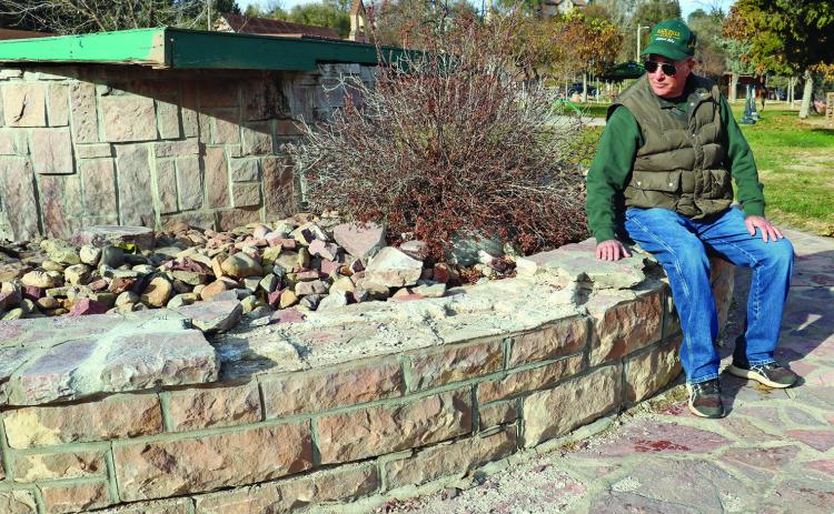 Gerald Collogan sits on the edge of the fountain in Centennial Park, near where much of the flagstone has broken away on its circular cap and is in need of repairs. Photo by Brett Nachtigall/Fall River County Herald-Star