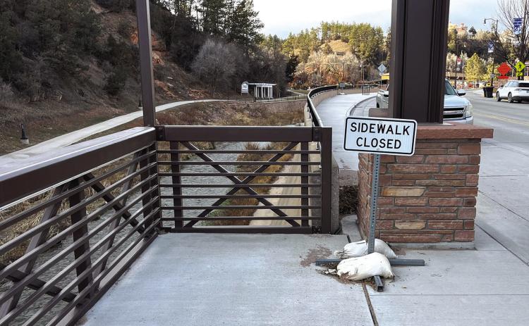 A ‘Sidewalk Closed” sign sits on the north end of the downtown suspended sidewalk due to a design flaw that placed a tower directly in the middle of the transition point leading to the regular sidewalk on the west side of North River Street. Photo by Brett Nachtigall/Fall River County Herald-Star