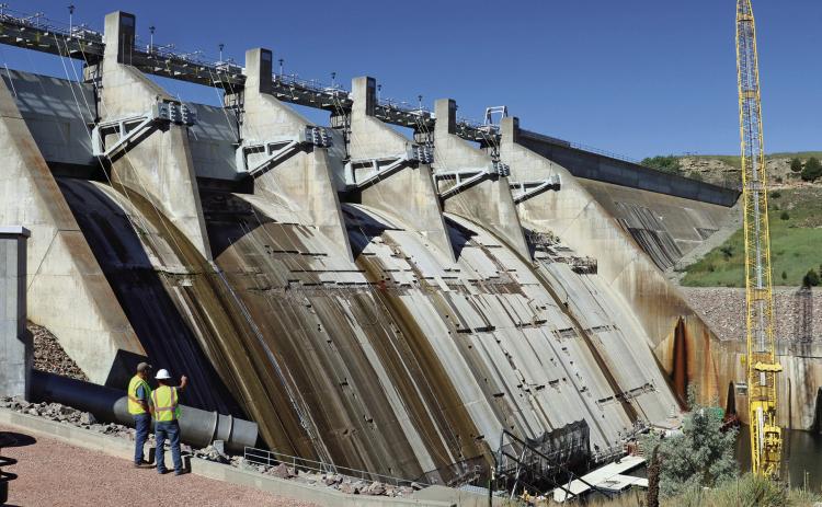 Angostura Dam Tender R.J. Wright, lower left, and Steven Fritch with the U.S. Bureau of Reclamation, stand above the work area and observe crews repairing concrete on the face of the dam. Photo by Brett Nachtigall/Fall River County Herald-Star