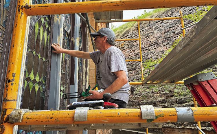 Tracy Wallach, of Classic Glass Ltd, sands and repairs the wood trim around each glass pane prior to painting and installing insulated double paned windows. Photo by Charity Maness / Fall River County Herald Star