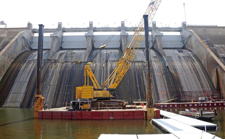 A large crane sits on a floating barge below Angostura Dam as workers come down on a scaffolding system (lower right) as part of a $10.4 million U.S. Bureau of Reclamation project currently underway south of Hot Springs. The main purpose of the project is address freeze-thaw deterioration by removing and replacing damaged concrete on the face of the dam. Photo by Brett Nachtigall/Fall River County Herald-Star