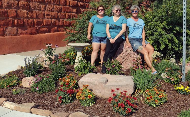 Keep Hot Springs Beautiful members Caitlyn Mosset, Christine Fraser and Shelley Hagans-Brown pose amongst the colorful flowers showcased in the bump-out located at the street corner across from Ace Hardware and in front of the Pioneer Building. This particular bumpout – one of 20 currently in the city – is being cared for by a group of neighbors who live in the Eagle Valley subdivision and call themselves the “Valley Girls.” Photo by Brett Nachtigall/Fall River County Herald-Star